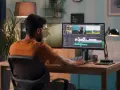 Hombre trabajando en la edición de video profesional en su estudio casero, con dos monitores mostrando la línea de tiempo y clips.