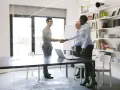 Un hombre sonríe mientras estrecha la mano de una mujer en una oficina. Un hombre mayor los observa. Quizás están discutiendo ingenierías con más salidas.
