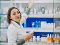 Farmacéutica con bata blanca revisa productos en estantería, un ejemplo de su futuro en el grado superior de farmacia.