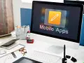 Escritorio de diseñador con ordenador mostrando "Mobile Apps", lápices de colores, gafas y cuadernos.