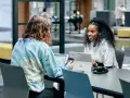 Dos estudiantes colaboran en un proyecto, discutiendo ideas mientras trabajan en sus laptops. Su trabajo en equipo es un ejemplo de cómo el **trabajo social** puede fomentar el aprendizaje y la innovación.