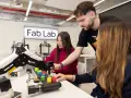 Estudiantes en un Fab Lab trabajan con un brazo robótico y bloques de colores, explorando la automatización y las relaciones internacionales.
