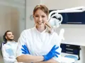 Sonrisa de profesional dental con guantes azules, lista para impartir un curso de higiene bucodental. Paciente relajado en silla dental al fondo.