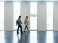 Dos estudiantes caminan por un pasillo moderno, quizás en una de las **biomedicina universidades**, con grandes ventanales y paredes de ladrillo blanco.