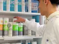 Un técnico superior en farmacia revisa productos en un estante, incluyendo geles de baño y desodorantes.