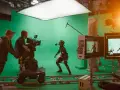 En un set de filmación con pantalla verde, un actor con traje de captura de movimiento interactúa con un equipo de filmación. Esto es vfx que es, la magia del cine.