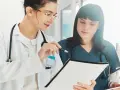 Dos médicas revisan documentación sanitaria a distancia homologado, una señala con un bolígrafo.