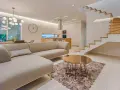 Elegante salón con sofá beige, mesa de centro dorada y alfombra circular. Escalera moderna de madera y cristal. La diferencia entre decorador y diseñador de interiores se refleja en la armonía del espacio.