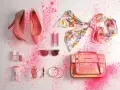 Zapatos, bolso, pañuelo, labiales, gafas de sol y accesorios de moda salpicados de polvo rosa.