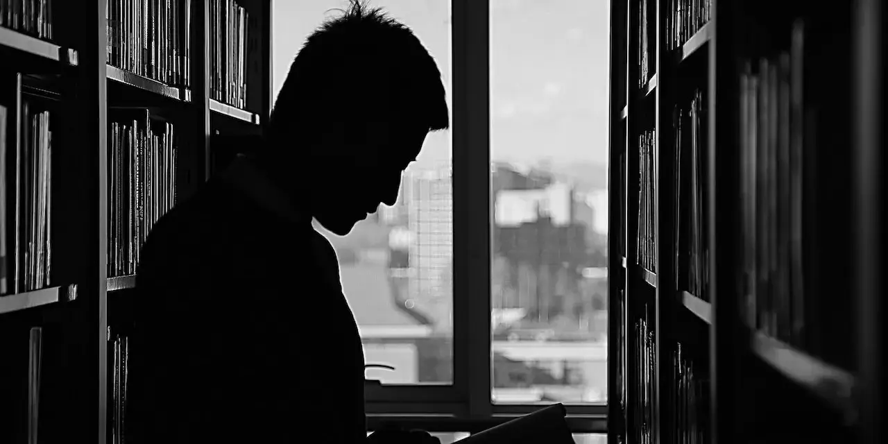 Silueta de un joven leyendo entre estanterías, buscando inspiración para sus futuras salidas de derecho.