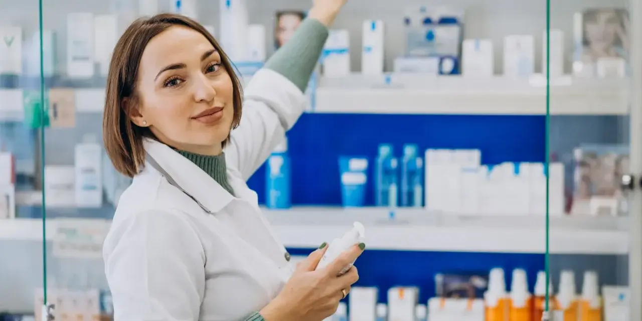 Farmacéutica con bata blanca revisa productos en estantería, un ejemplo de su futuro en el grado superior de farmacia.