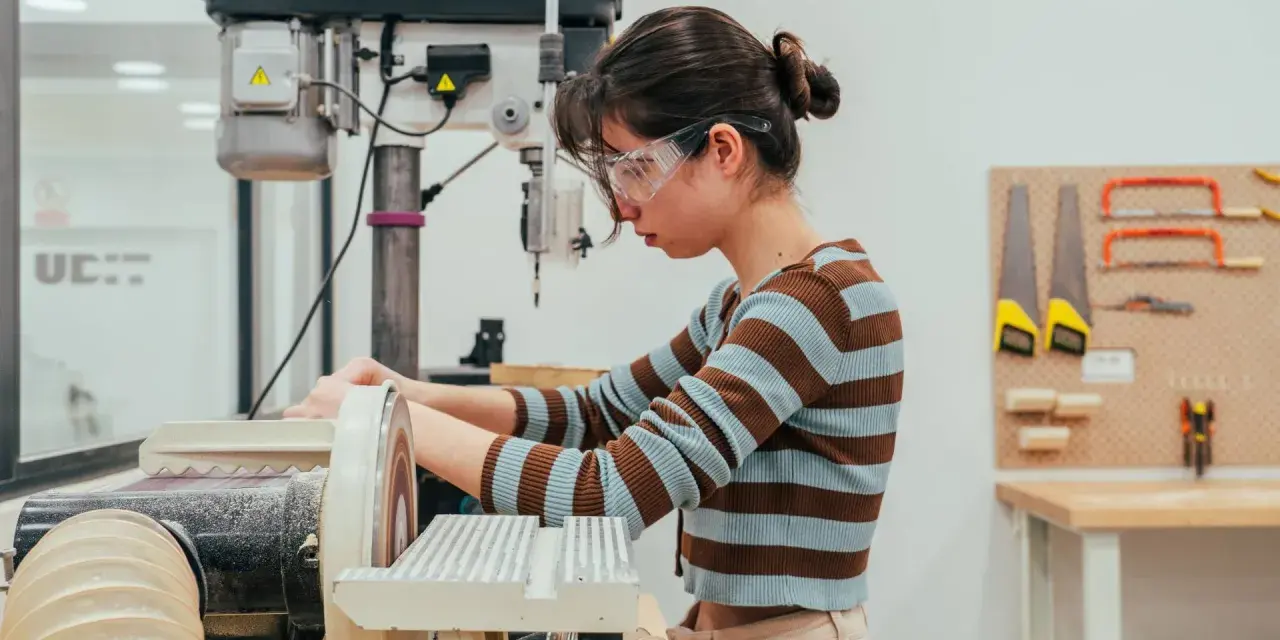 Joven en taller de ingeniería diseño industrial, concentrada en lijadora.