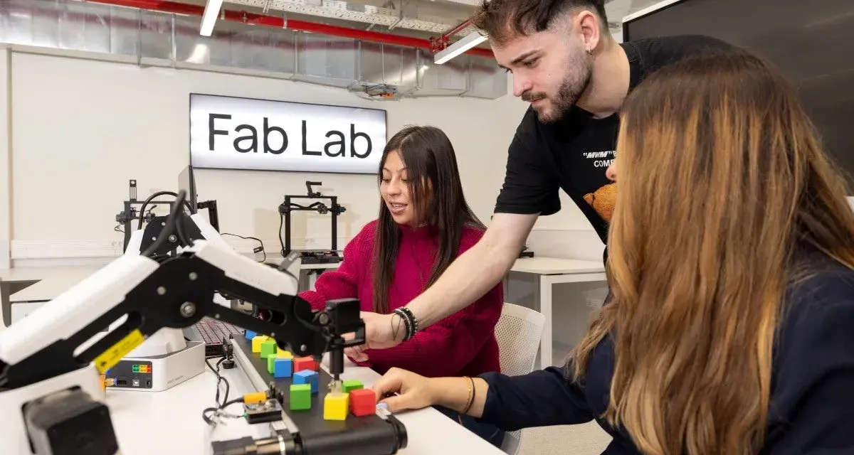 Estudiantes en un Fab Lab trabajan con un brazo robótico y bloques de colores, explorando la automatización y las relaciones internacionales.