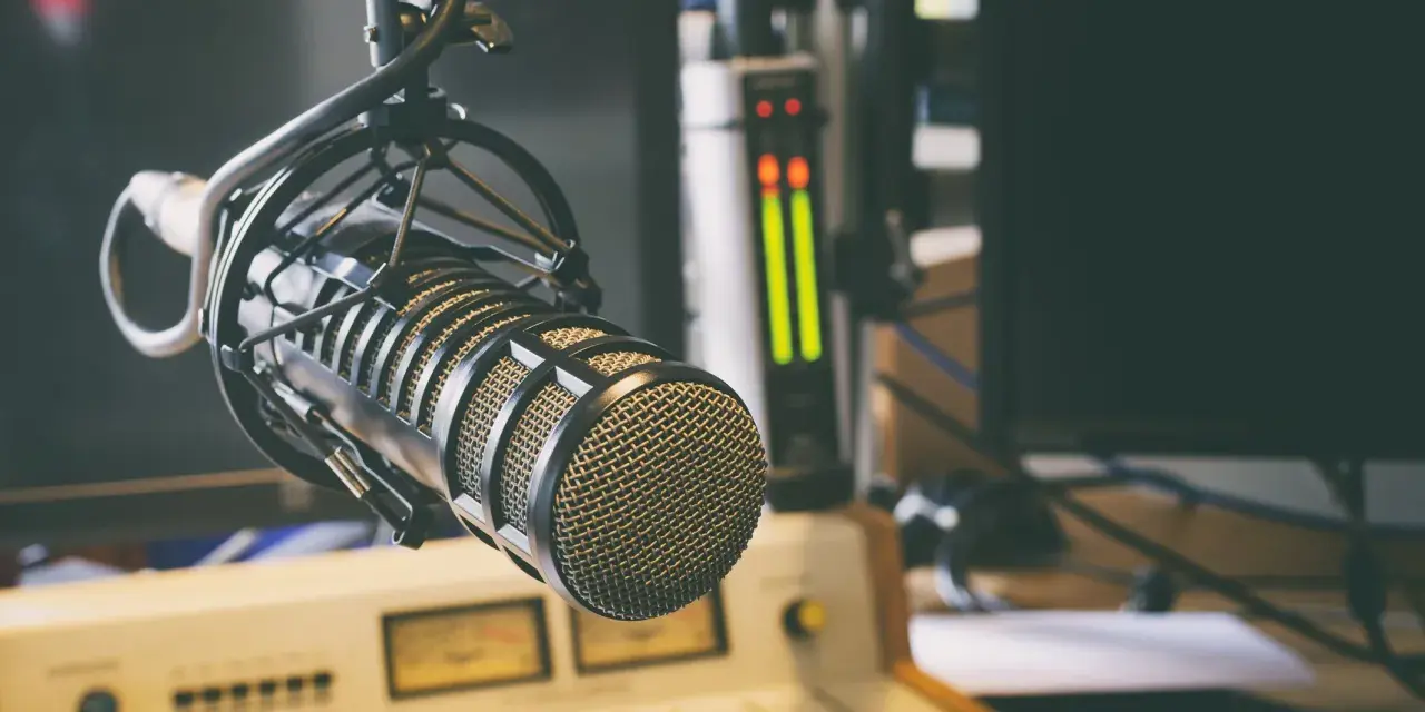 Micrófono profesional en estudio, listo para la comunicación audiovisual. Salidas de audio y consola de mezcla en el fondo.