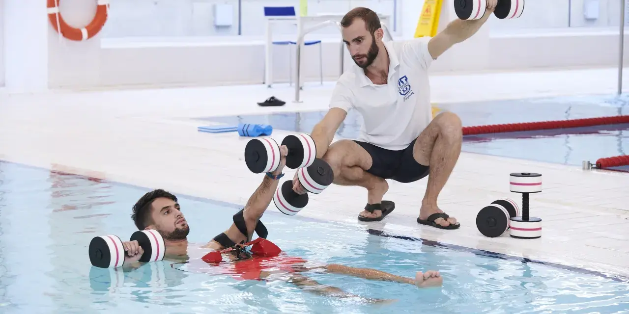 Un instructor guía a un paciente en fisioterapia acuática con pesas. Consulta el precio de fisioterapia en universidad privada para tu recuperación.