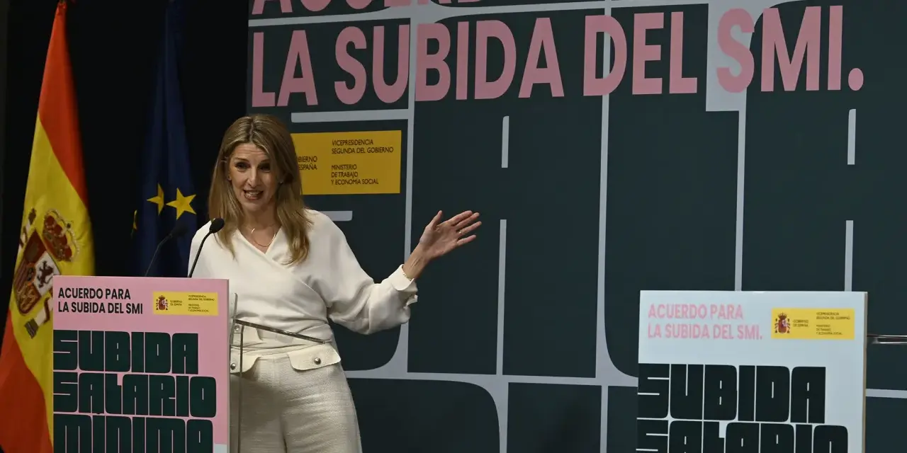 Una mujer habla en un podio con el lema "Acuerdo para la subida del SMI". Se discute cuánto cobra un trabajador social.