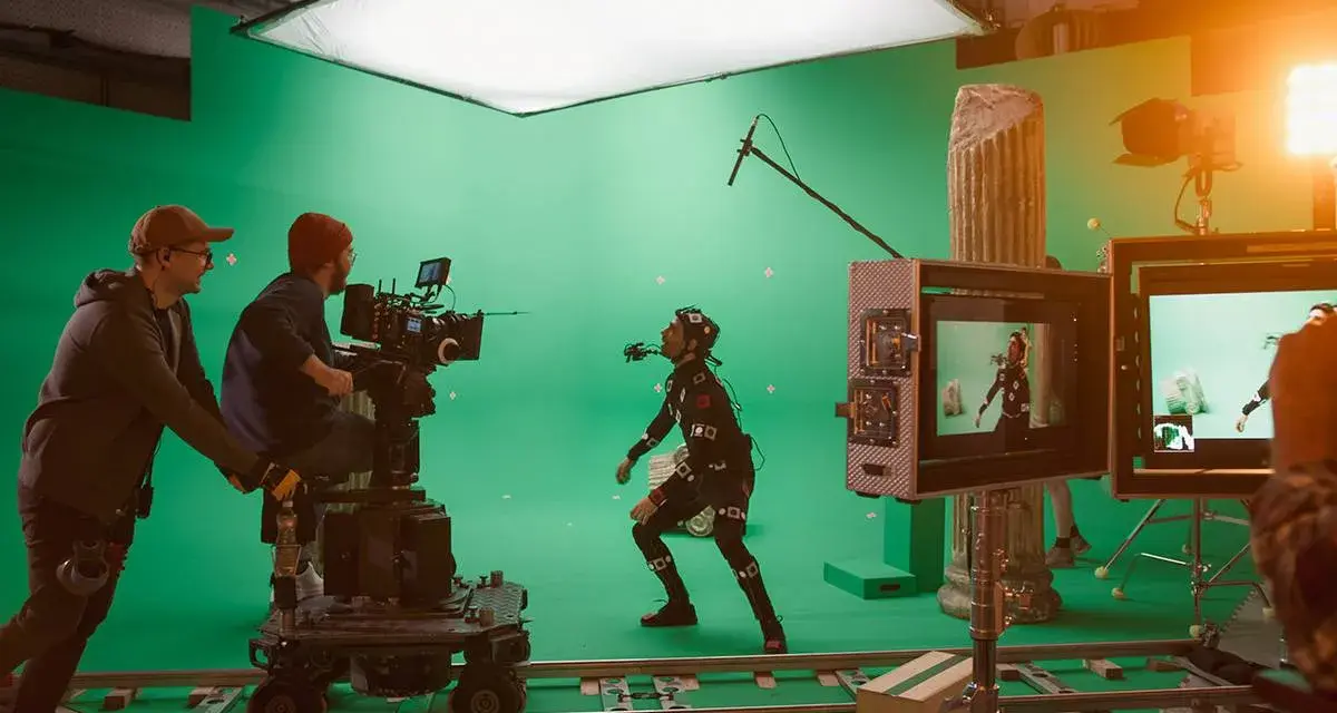 En un set de filmación con pantalla verde, un actor con traje de captura de movimiento interactúa con un equipo de filmación. Esto es vfx que es, la magia del cine.