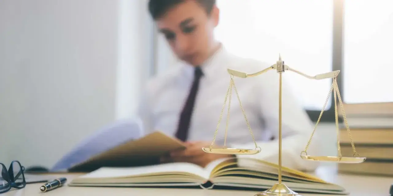 Estudiante de derecho concentrado en sus estudios, con una balanza de la justicia y libros. Averigua cuanto dura la carrera de derecho.
