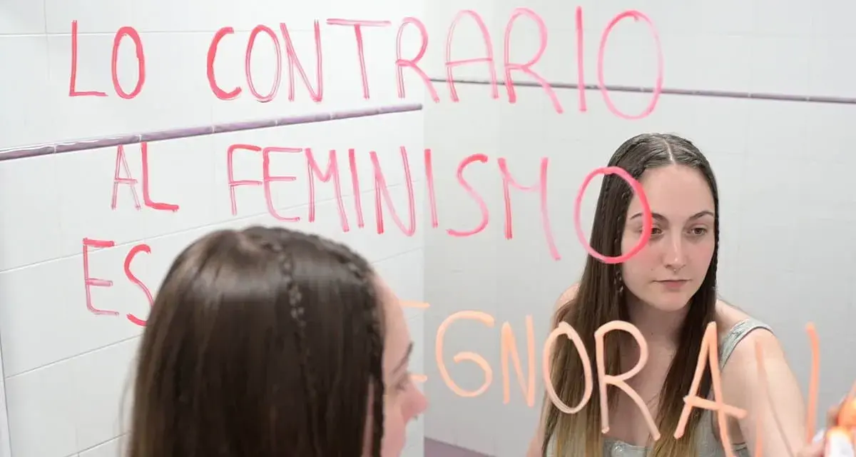 Joven reflexiona ante el espejo, escribiendo "Lo contrario al feminismo es ignorancia". Un mensaje para quienes estudian técnico superior en promoción de igualdad de género online.