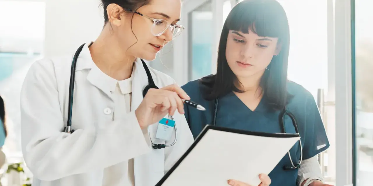 Dos médicas revisan documentación sanitaria a distancia homologado, una señala con un bolígrafo.