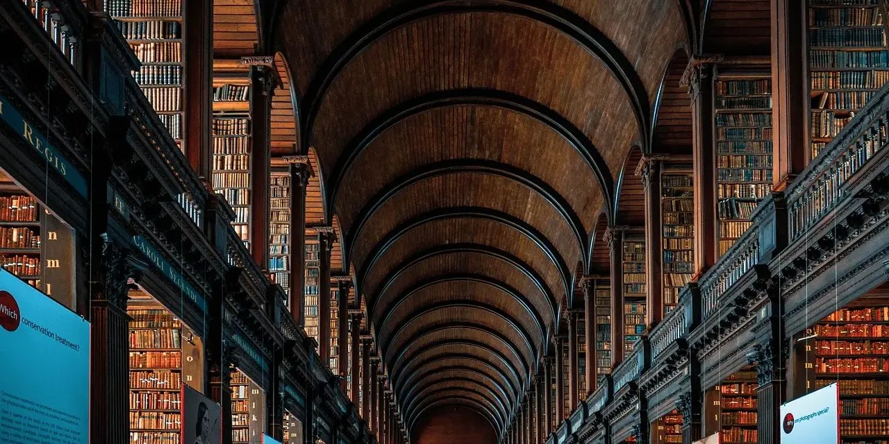 Pasillos de una biblioteca antigua con estanterías de madera repletas de libros, un ejemplo de la majestuosidad que se estudia en arquitectura.