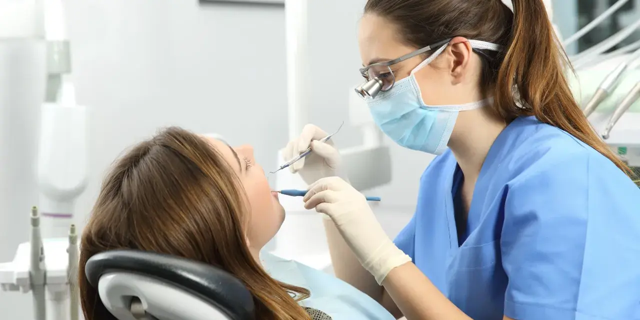 Dentista revisa la boca de una paciente. ¿Cuántos años son la carrera de odontología?