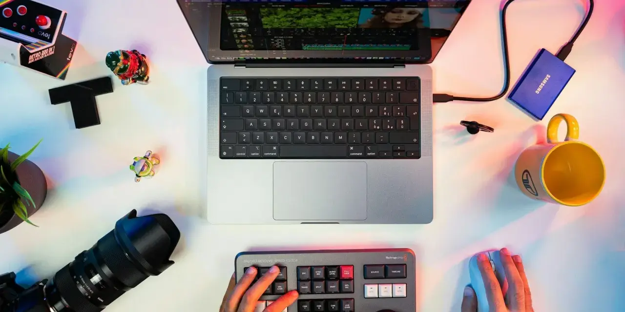 Un escritorio con un portátil mostrando un editor de video, un teclado de control, cámara, disco duro y taza. Ideal para los mejores editores de video para PC.