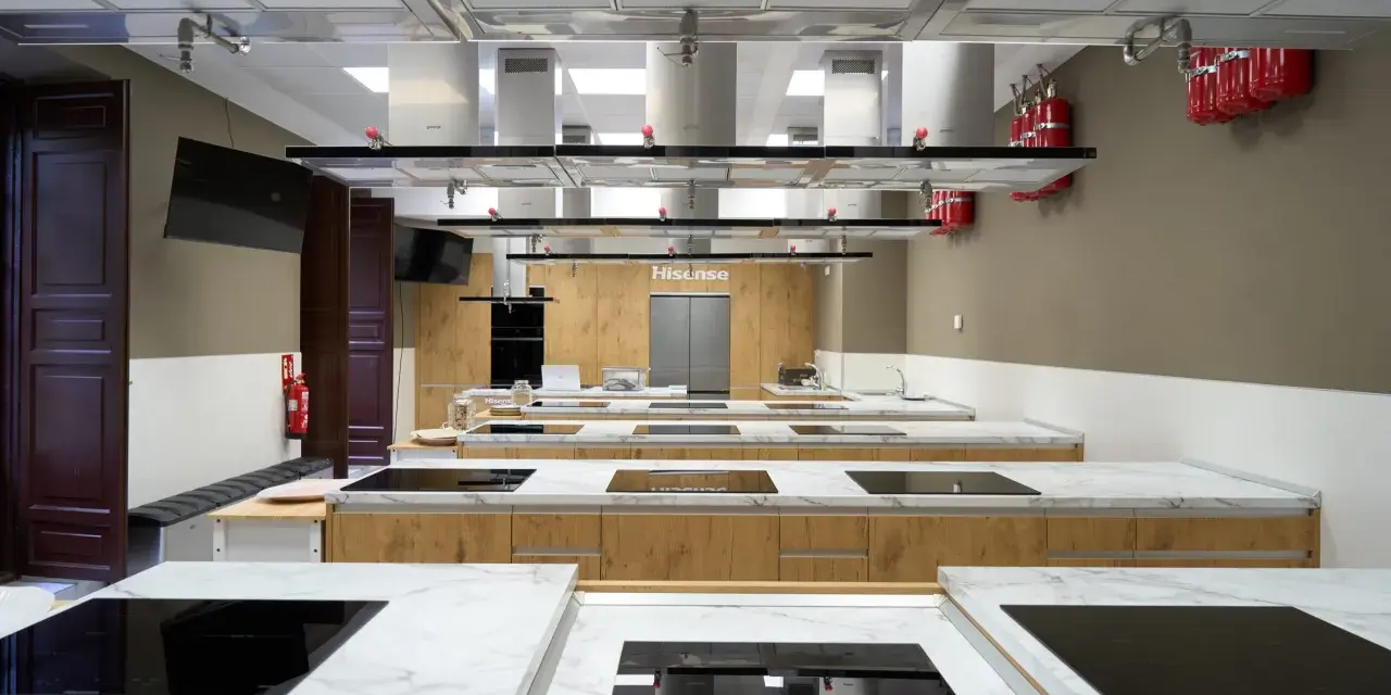 Cocina moderna equipada para una carrera de gastronomía, con encimeras de mármol, placas de inducción y campanas extractoras.