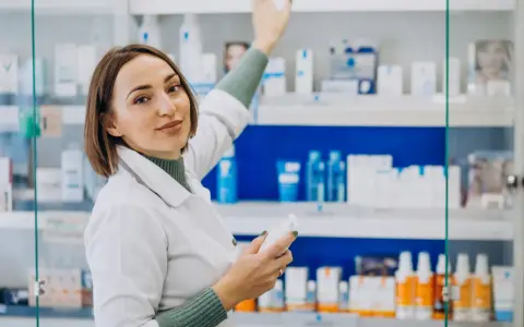 Farmacéutica con bata blanca revisa productos en estantería, un ejemplo de su futuro en el grado superior de farmacia.