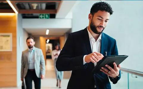 Hombre de negocios revisa su tablet, preparándose para sus dobles grados con relaciones internacionales.
