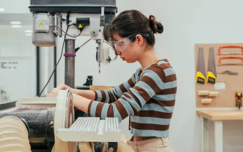Joven en taller de ingeniería diseño industrial, concentrada en lijadora.