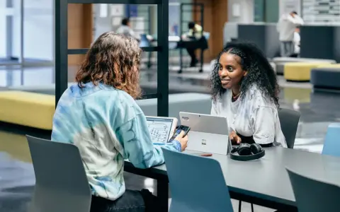 Dos estudiantes colaboran en un proyecto, discutiendo ideas mientras trabajan en sus laptops. Su trabajo en equipo es un ejemplo de cómo el **trabajo social** puede fomentar el aprendizaje y la innovación.
