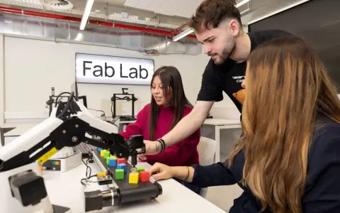 Estudiantes en un Fab Lab trabajan con un brazo robótico y bloques de colores, explorando la automatización y las relaciones internacionales.
