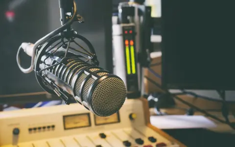 Micrófono profesional en estudio, listo para la comunicación audiovisual. Salidas de audio y consola de mezcla en el fondo.