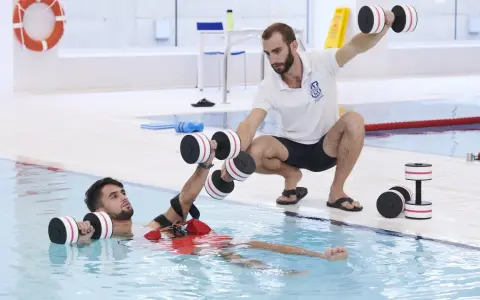 Un instructor guía a un paciente en fisioterapia acuática con pesas. Consulta el precio de fisioterapia en universidad privada para tu recuperación.