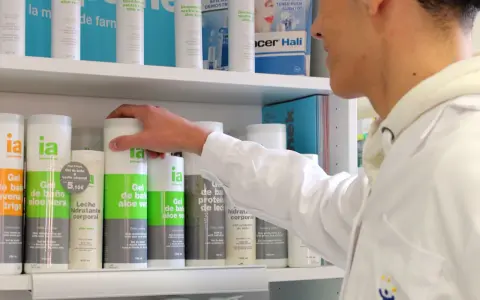 Un técnico superior en farmacia revisa productos en un estante, incluyendo geles de baño y desodorantes.
