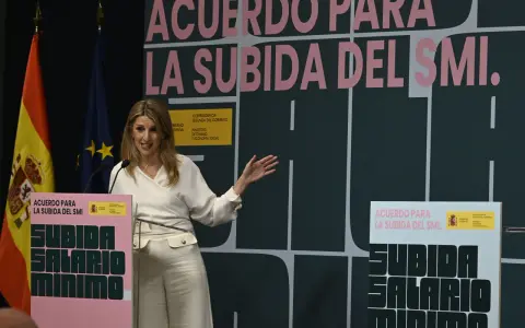 Una mujer habla en un podio con el lema "Acuerdo para la subida del SMI". Se discute cuánto cobra un trabajador social.