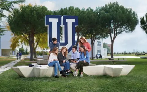 Estudiantes discuten en el campus de la Universidad Francisco de Vitoria, rodeados de árboles y el logo de la institución. Buenas **universidad francisco de vitoria opiniones** para elegir tu futuro.