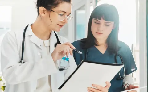 Dos médicas revisan documentación sanitaria a distancia homologado, una señala con un bolígrafo.