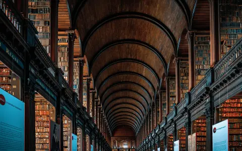 Pasillos de una biblioteca antigua con estanterías de madera repletas de libros, un ejemplo de la majestuosidad que se estudia en arquitectura.