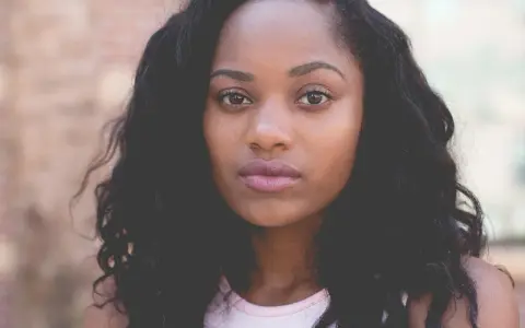 Primer plano de una mujer joven con cabello oscuro y rizado, ojos marrones y labios rosados. Imágenes de personas sin derechos de autor.