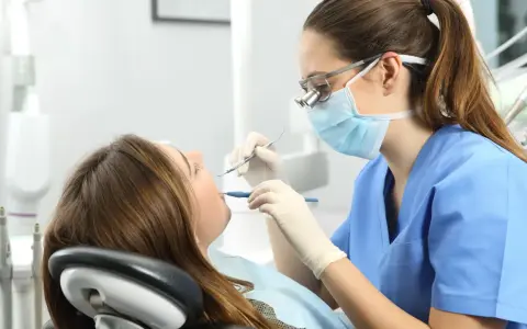 Dentista revisa la boca de una paciente. ¿Cuántos años son la carrera de odontología?