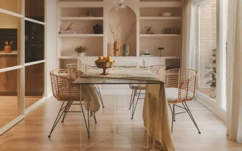 Comedor moderno con mesa de cristal y sillas de ratán. Estanterías empotradas y un toque de diseño de interiores cálido.
