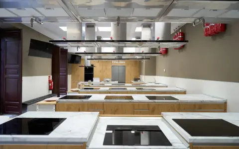 Cocina moderna equipada para una carrera de gastronomía, con encimeras de mármol, placas de inducción y campanas extractoras.