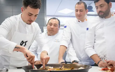 Cuatro chefs observan atentamente una paella. Se debate la diferencia entre chef y cocinero mientras preparan el plato.
