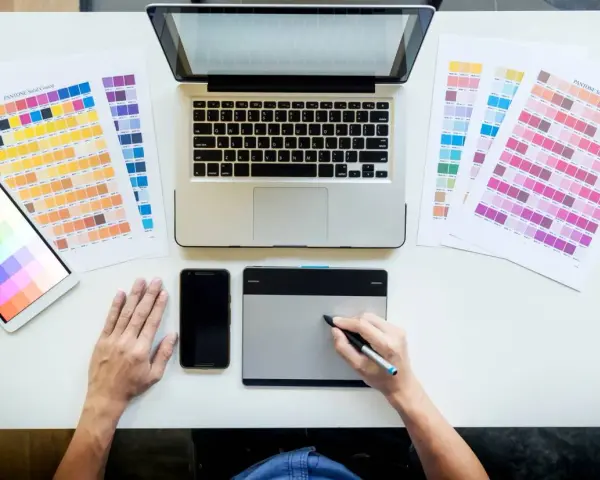 Diseñador gráfico trabajando en su escritorio con paletas de colores, tablet, móvil y portátil. Así se ve el día a día de cuanto gana un diseñador gráfico.