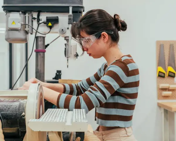 Joven en taller de ingeniería diseño industrial, concentrada en lijadora.