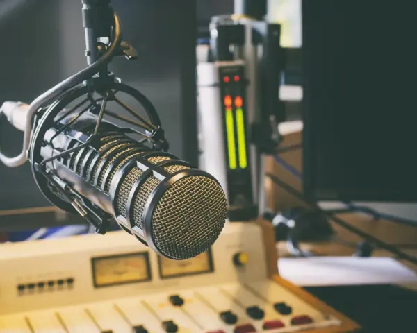 Micrófono profesional en estudio, listo para la comunicación audiovisual. Salidas de audio y consola de mezcla en el fondo.