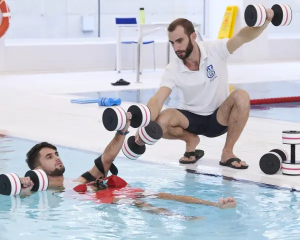 Un instructor guía a un paciente en fisioterapia acuática con pesas. Consulta el precio de fisioterapia en universidad privada para tu recuperación.