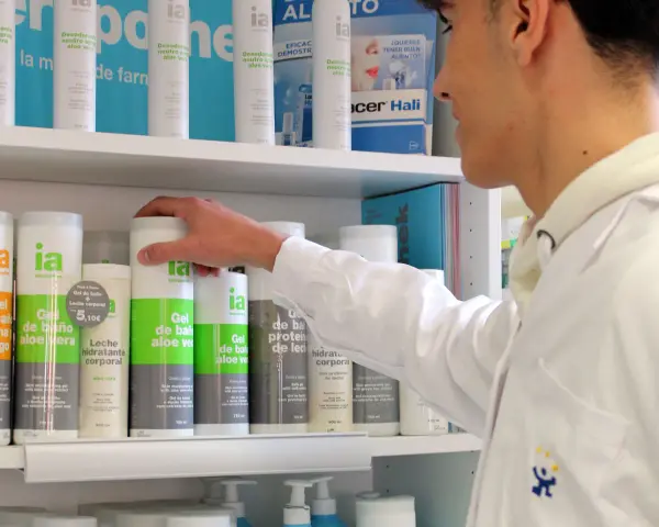 Un técnico superior en farmacia revisa productos en un estante, incluyendo geles de baño y desodorantes.
